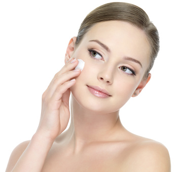 Portrait of young woman applying moisturizer cream on her pretty face - white background